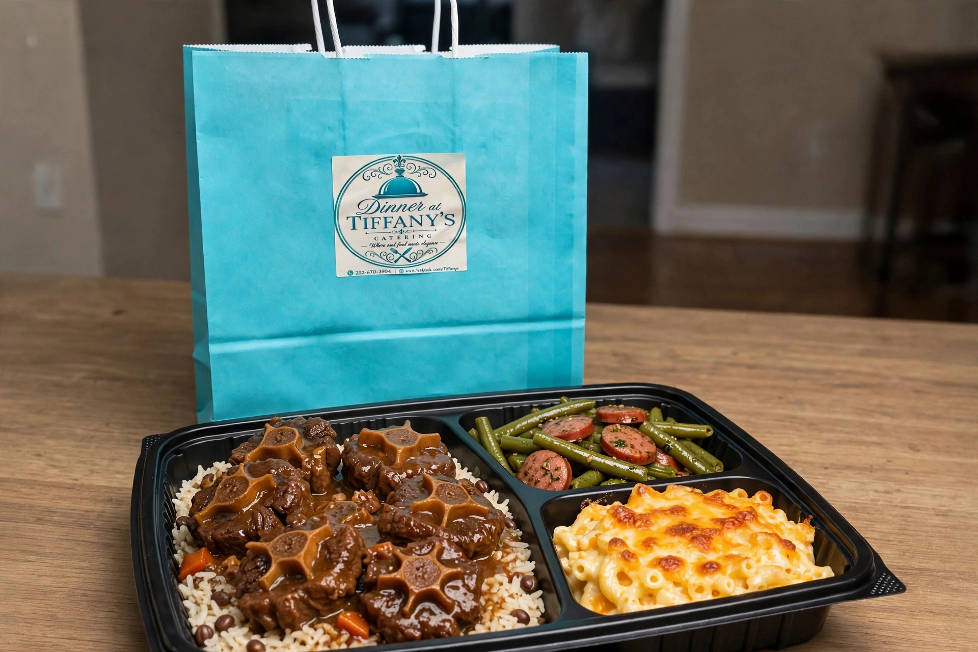 Braised oxtails over jasmine rice with green beans and mac and cheese in a takeout container with the full Tiffany blue bag and its handles showing